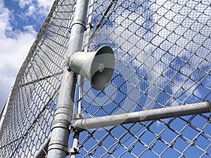 Low angle view of an announcer speaker attached to a fence at a ball park on a bright, sunny day