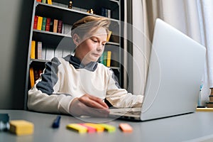 Low-angle view of astonished pupil boy using typing laptop doing online lesson via Internet at desk, selective focus.