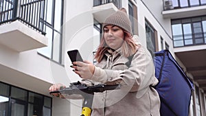 Low-angle view of attractive adult female courier browsing address on mobile phone map app standing outdoors.