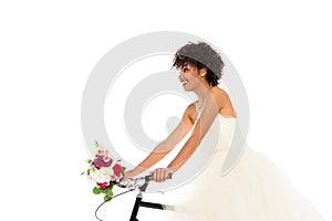 Low angle view of attractive african american bride in wedding dress holding flowers while riding bicycle