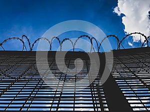 Low angle view of barbed wire fence prison, airport against a backdrop of clear blue sky with a single white cloud.