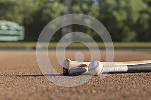 Low angle view of a baseball and bats on dirt infield of baseball park in afternoon sunlight