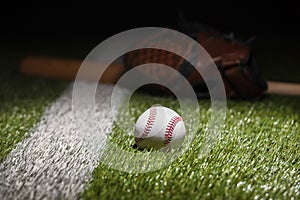 Low angle view of baseball on grass field with stripe and defocused mitt and bat