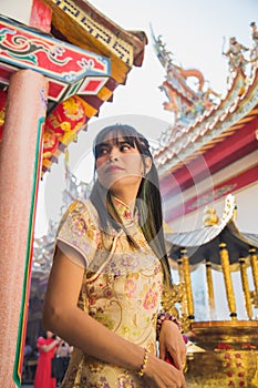 Low angle view beautiful Asian woman wearing a yellow traditional cheongsam qipao dress holding red hand fan looking at side in