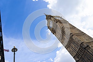 ALow angle view of the Big Ben in London England United Kingdom against a blue sky with white clouds and a Union Jack British flag