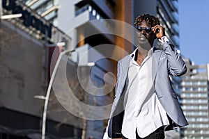 Low angle view of a black african young man wearing elegant clothes with sunglasses put in on eyeglasses while walking on the