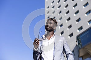 Low angle view of black african young man wearing elegant clothes with sunglasses put in on eyeglasses while walking on the street