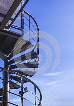 Low angle view of black metal spiral staircase outside of modern house building against blue sky background