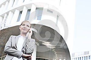 Low angle view of businesswoman using cell phone outside office building