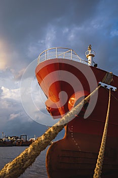 Low angle view of cargo ship docked at port against rain cloudy sky at sunset time