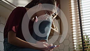 Low angle view of caucasian teenager girl sitting in the kitchen and using mobile phone in silence