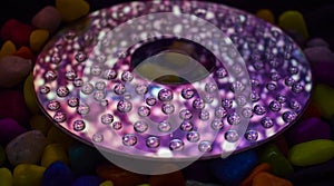 Low angle view of a CD ROM with water droplets on it and coloured stones in the background.
