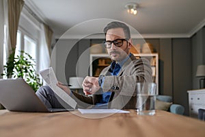 Low angle view of confident businessman checking time on wristwatch while working in home office.
