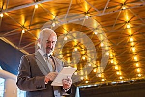 Low angle view of confident senior businessman using digital tablet while standing against illuminated roof