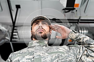 low angle view of confident soldier in military uniform saluting
