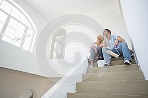 Low angle view of couple with painting tools sitting on steps in new house