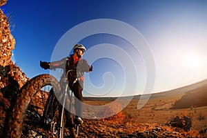 Low angle view of cyclist riding mountain bike on rocky trail at sunrise