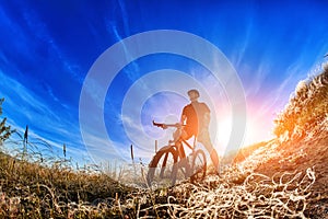 Low angle view of cyclist standing with mountain bike on trail at sunrise.