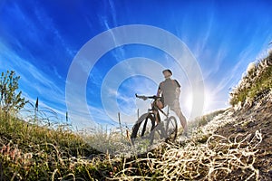 Low angle view of cyclist standing with mountain bike on trail at sunrise.