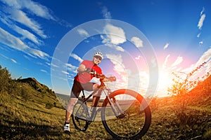 Low angle view of cyclist standing with mountain bike on trail at sunset