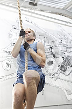 Low angle view of determined man climbing rope in crossfit gym