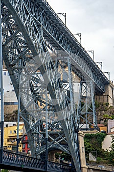 Low angle view of the Don Luis I steel bridge in Porto and people walking and taking photos of the Douro River on the upper