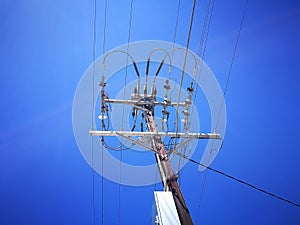 A Low angle view of Electricity High Voltage Transformer for Sending Power Line Energy Generation isolated on blue sky background.