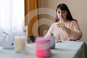 Low-angle view of female craftswoman preparing using of scented oil for creating candle building mixture. Process of