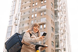 Low-angle view of food delivery woman courier with thermal bag and electric scooter, lost in city and using navigation