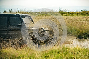 Low angle view of front of SUV on mountain road. Off-road Jeep car on bad gravel road. Mud and water splash in off-road