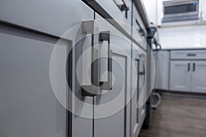 Low angle view of gray kitchen cabinet door handles inside a large, beautiful kitchen with finished, hardwood floors