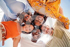 Low angle view of a group of five multiracial teenagers smiling and looking down at camera outdoors. Young student