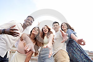 Low angle view of a group of multiracial friends looking at camera and smiling while enjoying time together outdoors.