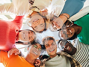 Low angle view of a group of multiracial friends standing on a circle, smiling and embracing together. Young teenagers