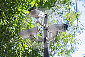 Low angle view group of the surveillance security cameras or CCTV with sunlight on steel pole in outdoor public car parking with