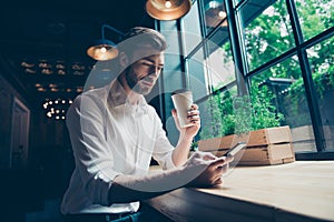 Low angle view of a handsome brunet guy entrepreneur having a coffee break in a loft styled restaurant, looking serious, well dres