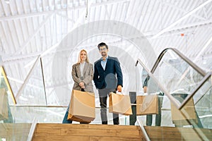 Low-angle view of happy beautiful young couple holding shopping paper bags with purchases and looking at camera