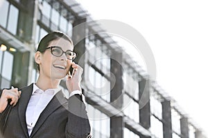 Low angle view of happy businesswoman using cell phone outside office building