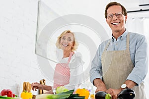 low angle view of happy senior couple cooking together at kitchen and looking