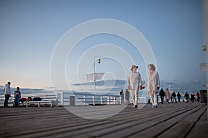 Low angle view of happy senior couple in love on walk outdoors on pier by sea at dusk, holding hands.