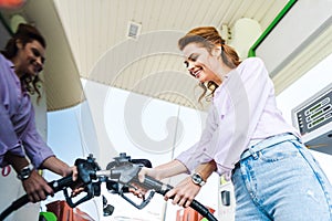 Angle view of happy woman holding fuel pump while refueling car with benzine photo