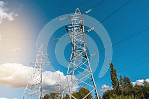 Low angle view of high voltage towers and electric cables against sunny blue sky