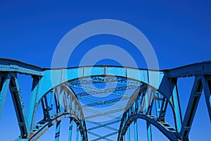 Low angle view on isolated symmetrical industrial steel bridge deck against blue sky with cross struts and metal beams