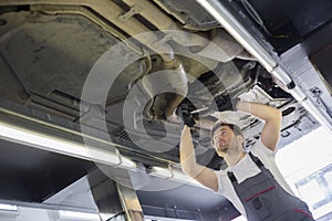 Low angle view of male automobile mechanic repairing car in repair shop