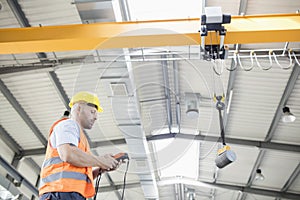 Low angle view of manual worker operating crane lifting steel in industry photo