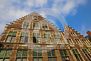 Low angle view on medieval brick stone house facade with typical belgian stepped gabled roof against blue sky with clouds -  Ghent