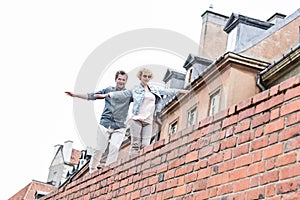 Low angle view of middle-aged couple with arms outstretched walking on brick wall against clear sky