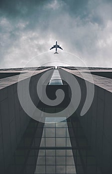 Low angle view of modern tall business building. Commercial jet plane flying over skyscraper. Against dramatic cloudy