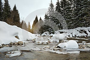 Low angle view - morning on river in winter, stones snow covered, coniferous trees and rising sun in distance