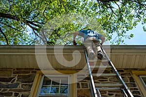 Low angle view of off center man on ladder cleaning gutters of a stone home